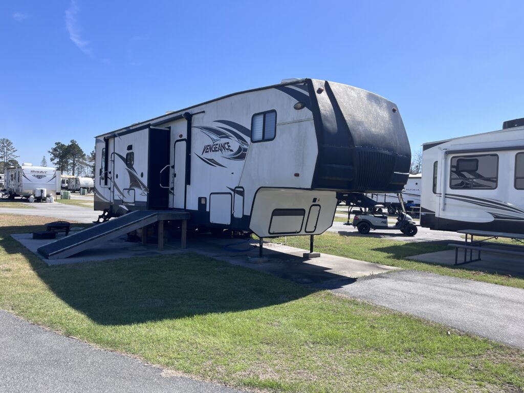 A parked Vengeance RV with a ramp, surrounded by other RVs in a sunny campground setting.