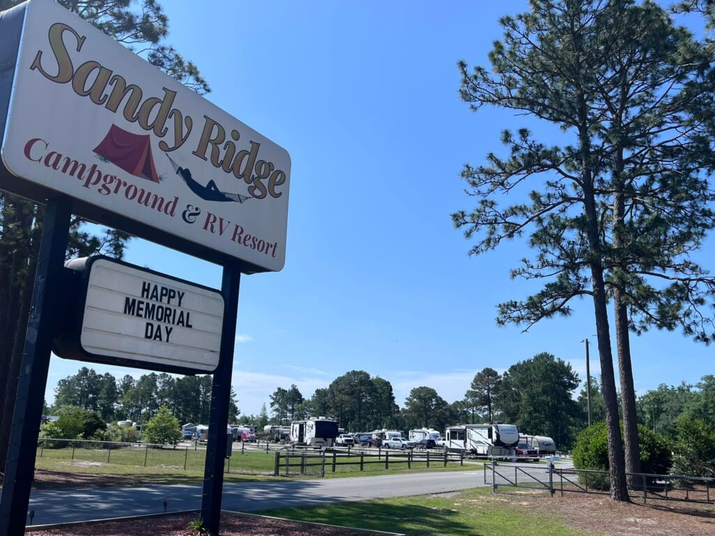 Sandy Ridge Campground and RV Resort sign with blue sky and trees, welcoming visitors on Memorial Day.