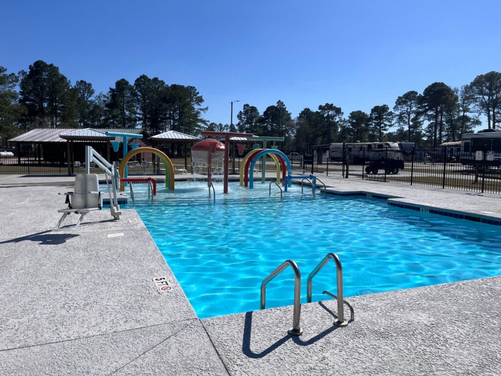 Bright and inviting swimming pool with colorful water slides and clear blue water, surrounded by trees and recreational facilities.