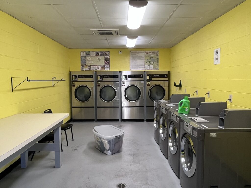 Bright laundry room featuring multiple washing machines, a folding table, and a basket of clothes on the floor.