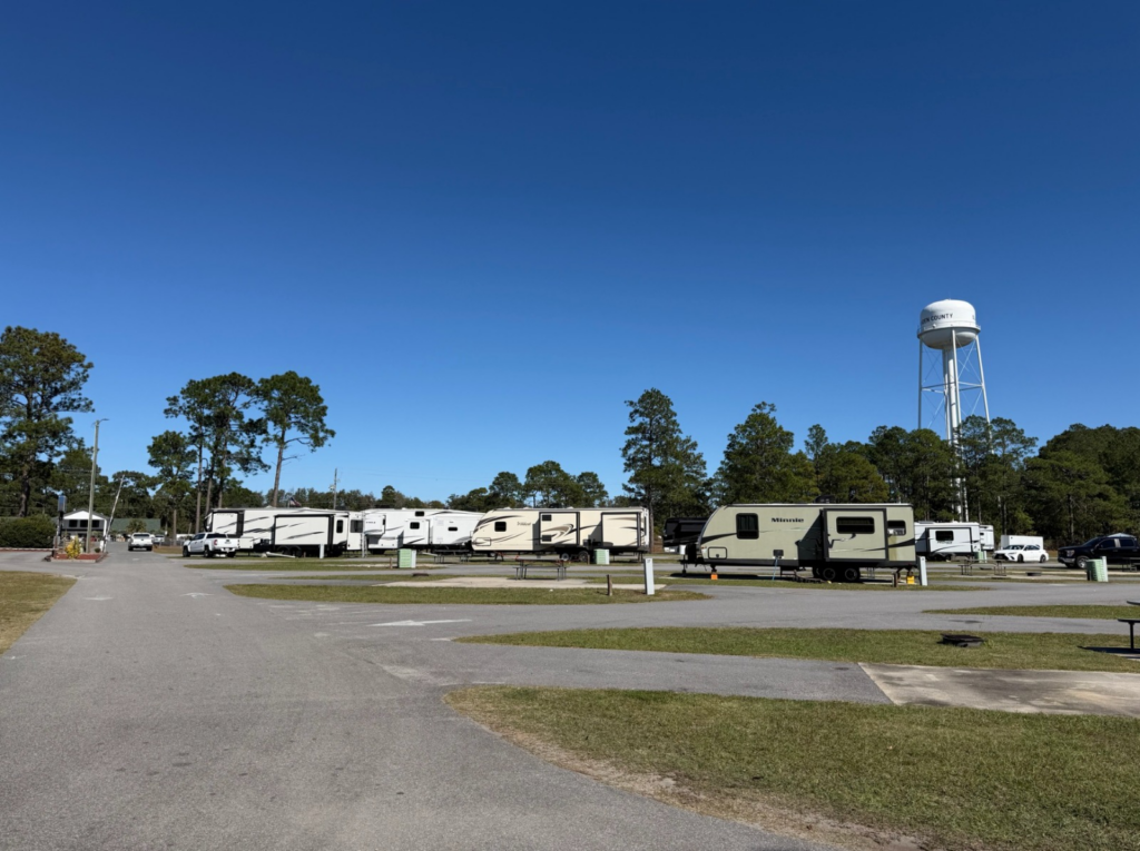 A scenic view of an RV park with several parked trailers and a water tower under a clear blue sky.