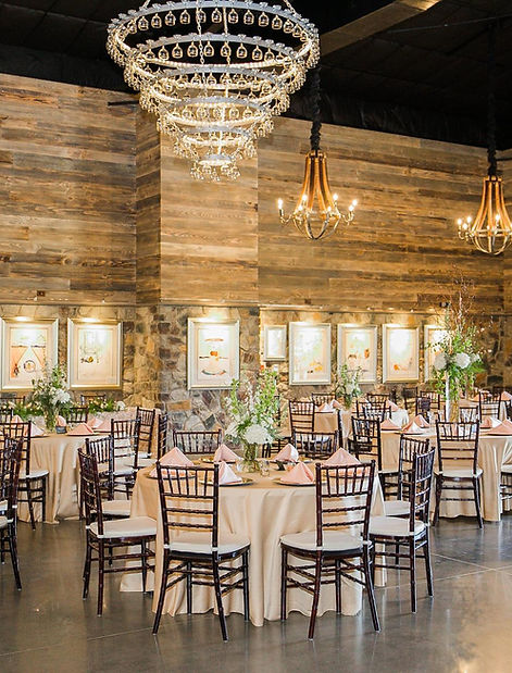 Elegant dining setup in a rustic venue with wooden walls, chandeliers, and beautifully arranged tables for an event.