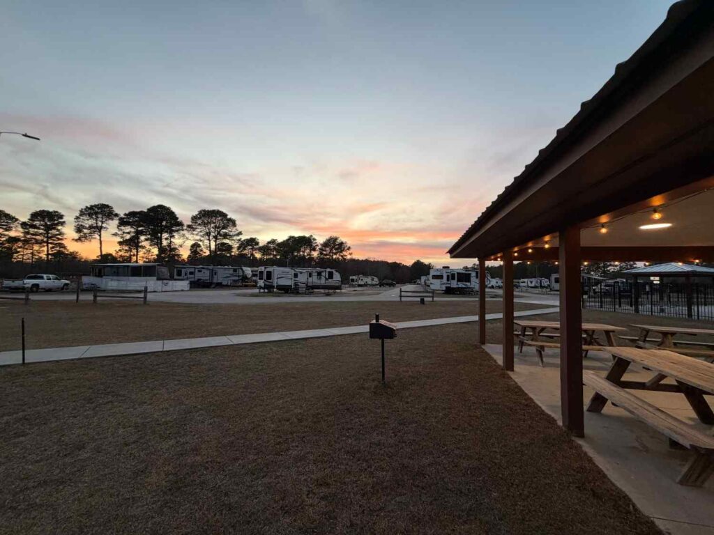 Scenic view of an RV park at sunset, featuring picnic tables and parked RVs under a colorful sky.