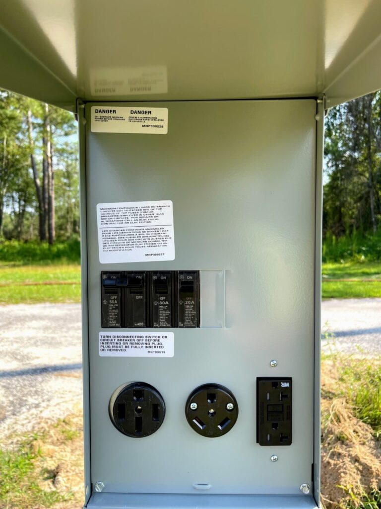 Electrical panel with circuit breakers and outlets, warning labels visible, set in a natural outdoor environment.